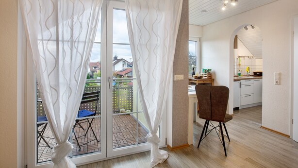 A room with a sliding glass door, a chair, a kitchen area, and a view of the outside. - Holiday Apartment 'Lueg Ins Wiesental' with Mountain View, Balcony & Wi-Fi (Steinen)