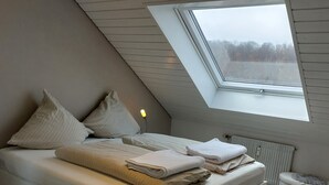 A modern loft bedroom with a sloped ceiling, a skylight, a bed with pillows and blankets, a bedside table with a lamp, and a radiator. - Holiday Apartment 'Lueg Ins Wiesental' with Mountain View, Balcony & Wi-Fi (Steinen)