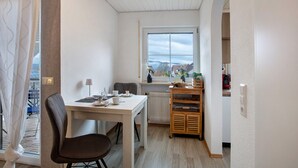 A small, well-lit room with a table, chairs, a radiator, and a view through a window. - Holiday Apartment 'Lueg Ins Wiesental' with Mountain View, Balcony & Wi-Fi (Steinen)