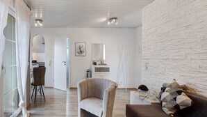 A modern living room with a stone wall, a brown sofa, a beige armchair, and a dining area in the background. - Holiday Apartment 'Lueg Ins Wiesental' with Mountain View, Balcony & Wi-Fi (Steinen)