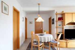 Ruokailutilassa on pyöreä pöytä, tuolit, riippuvalaisin ja televisio, joka on sijoitettu puiseen jalustaan.