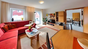 A modern living room with a red sofa, a coffee table, and a dining area with a wooden table and chairs. - Apartment 'Tannenblick 3-2' with Shared Garden, Balcony and Wi-Fi (Oberhof)