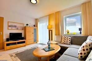 Una sala de estar moderna con televisor de pantalla plana, sofá, mesa de centro y ventana con cortinas.