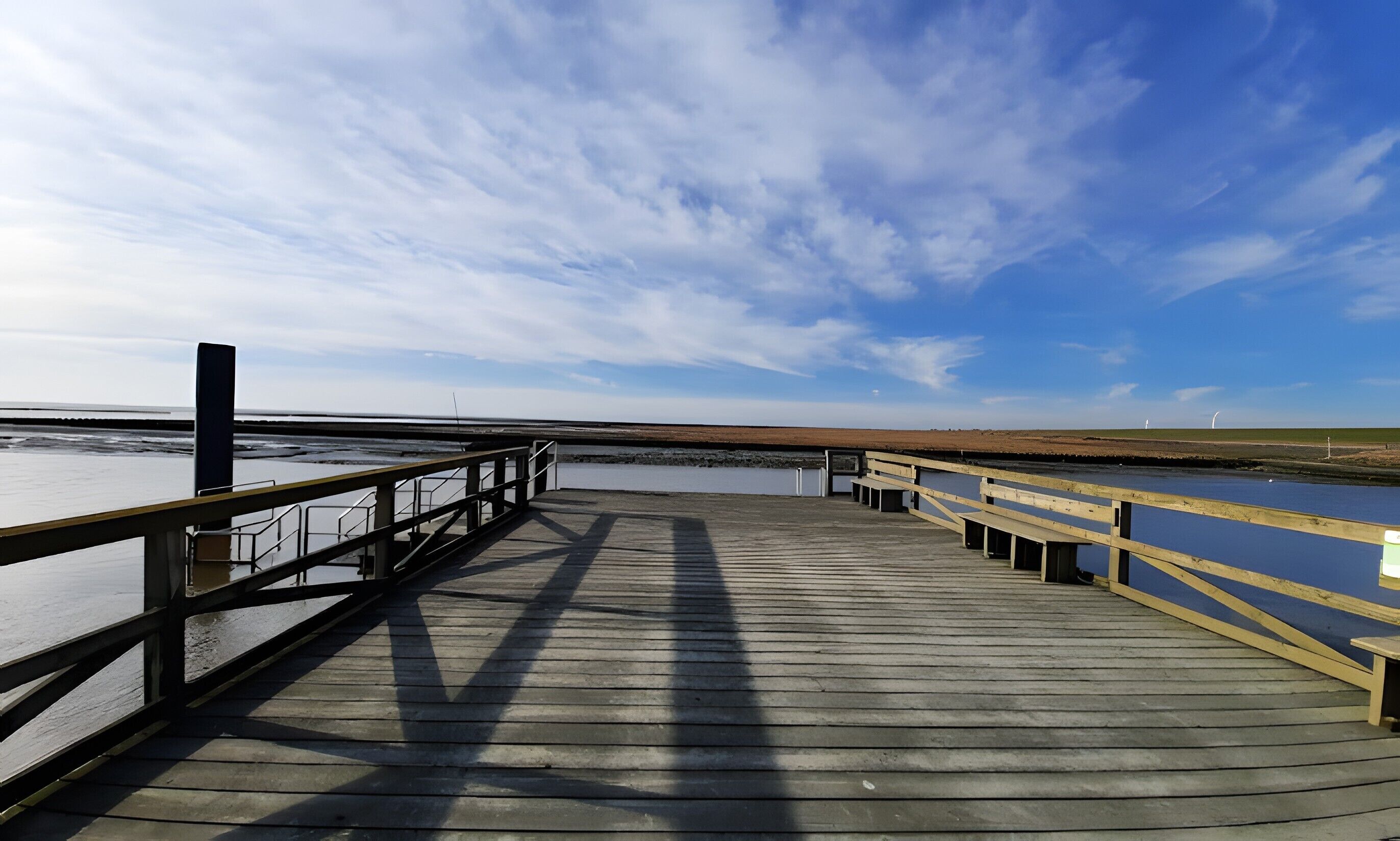 Ein Holzsteg führt zu einem Strand unter blauem Himmel.