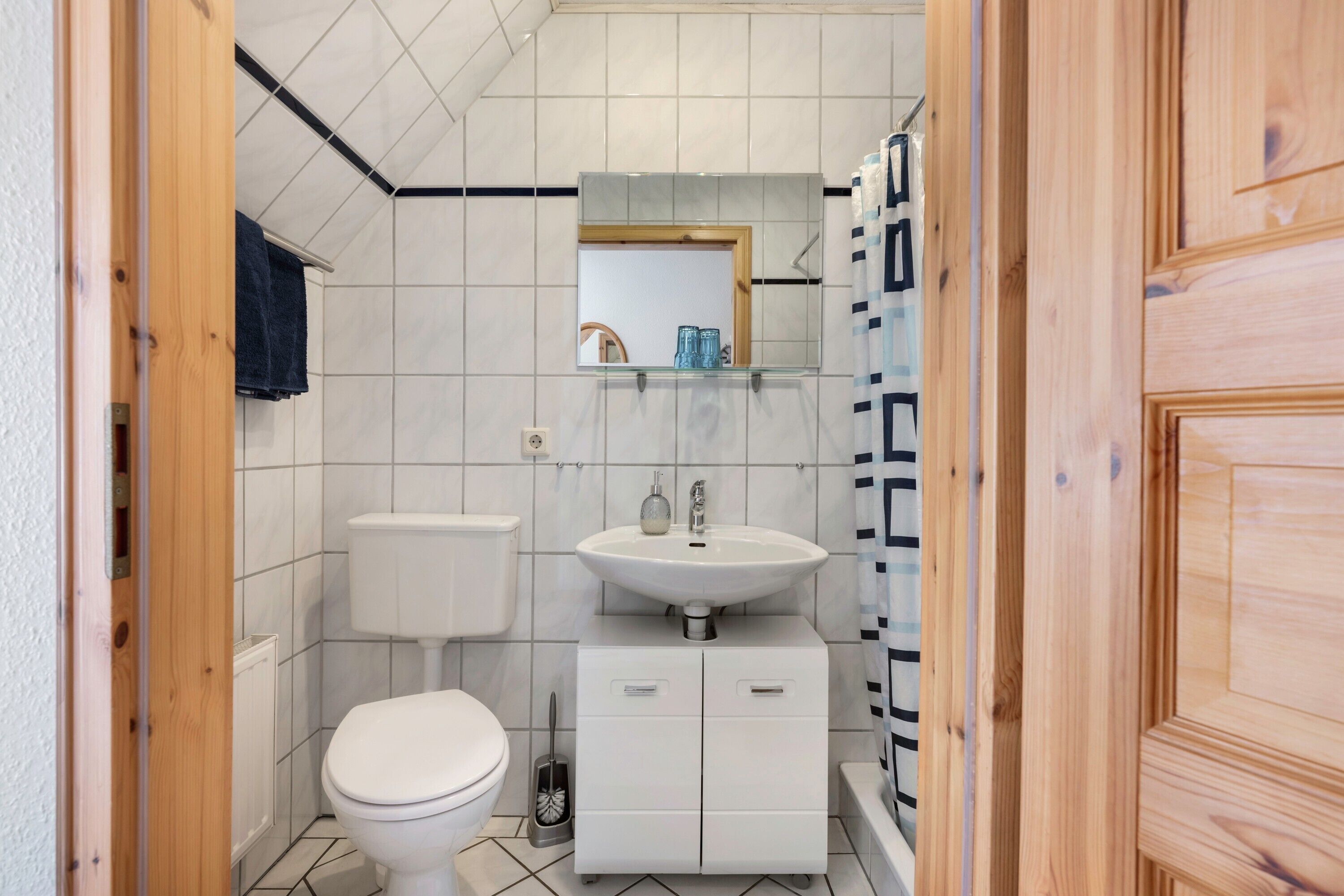 Ein kleines Badezimmer mit Toilette, Waschbecken und Schrank, mit Fliesenboden und Holztür.