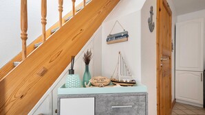 Una escalera con balaustres de madera, un cartel de bienvenida, una maqueta de barco y un mueble con un adorno.