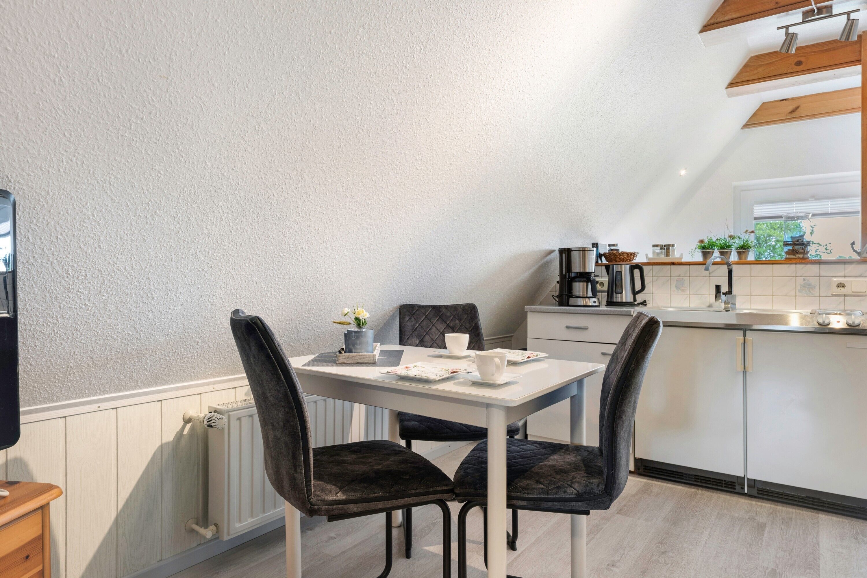 Une cuisine moderne avec une table blanche, des chaises foncées et un plan de travail blanc.