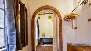 A bathroom with a brick archway, a bathtub, a wooden dresser, and a hanging plant. - Cosy apartment for 2 people with private pool, TV, patio and pets allowed (Barga)