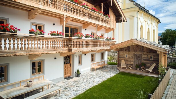 Un chalet traditionnel doté de balcons en bois, d’une cour pavée de pierres et d’un espace extérieur aménagé pour s’asseoir.