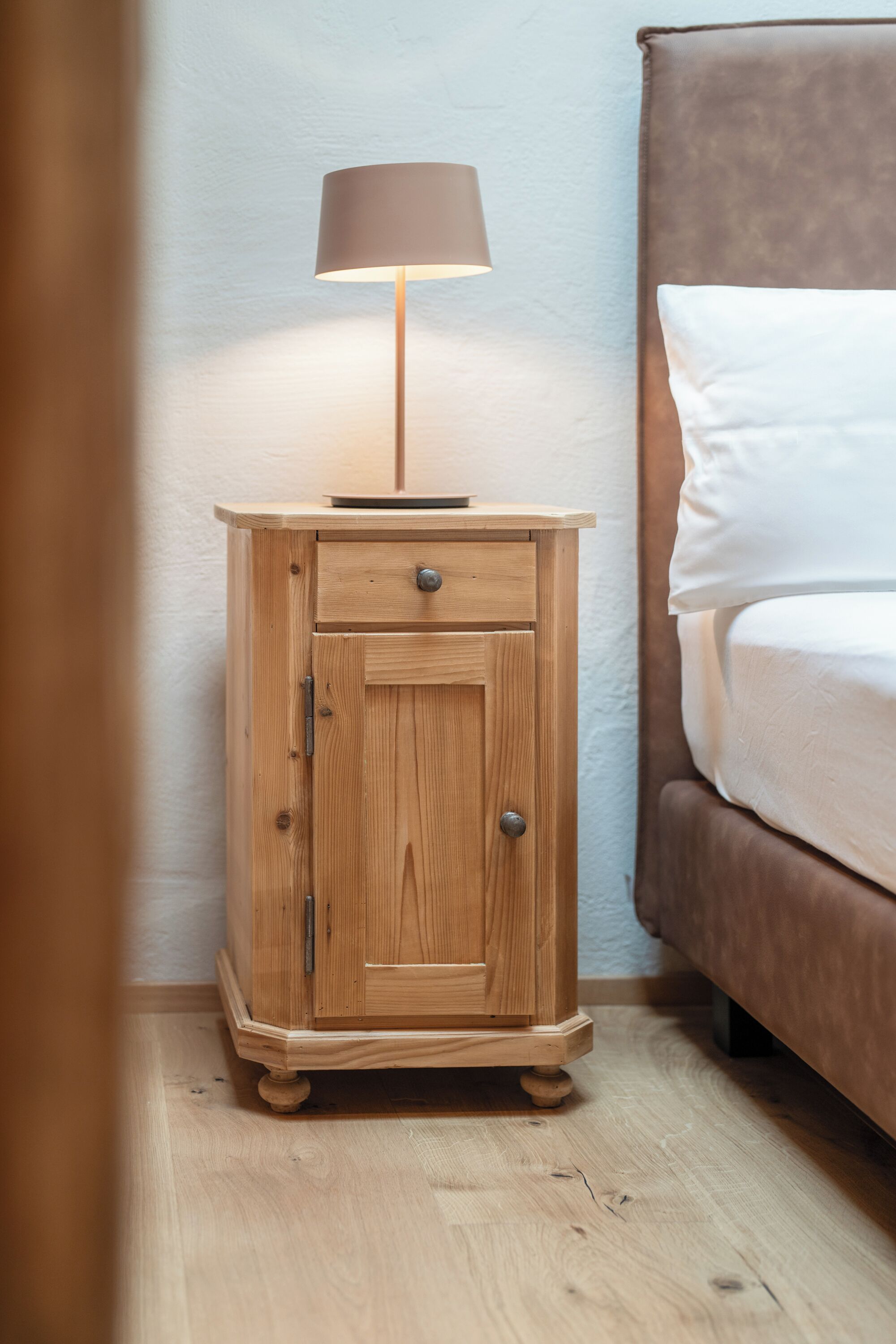 Een houten nachtkastje met een lamp, een lade en een kastje.