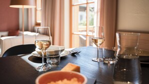 Une table à manger dressée avec des verres à vin, des assiettes et un saladier rempli de nourriture, une lampe et des rideaux en arrière-plan.