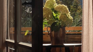 Une fenêtre donnant sur les montagnes et un vase rempli de fleurs.