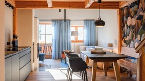A modern kitchen with wooden cabinets, a dining table with chairs, and a view of the living area with a sofa and a lamp.