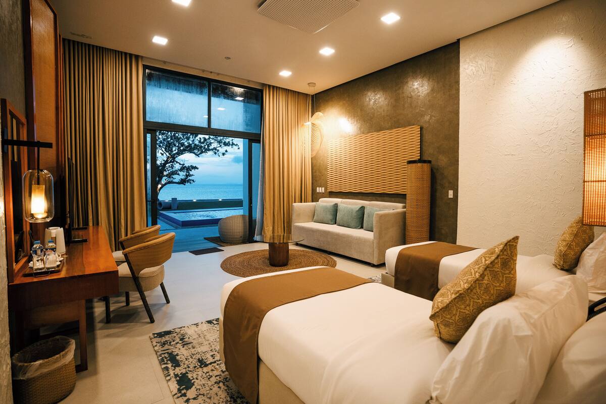 A hotel room with a bed, a sofa, a desk, and a view of the sea.