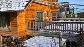 A wooden cabin with a sloped roof, a deck, and a view of a snowy landscape. - Vacation home cloverleaf 175sqm with balcony and terrace (Siegsdorf)