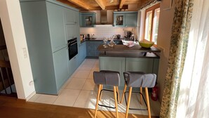 A kitchen with light blue cabinets, a wooden ceiling, and a large island with bar stools. - Vacation home cloverleaf 175sqm with balcony and terrace (Siegsdorf)