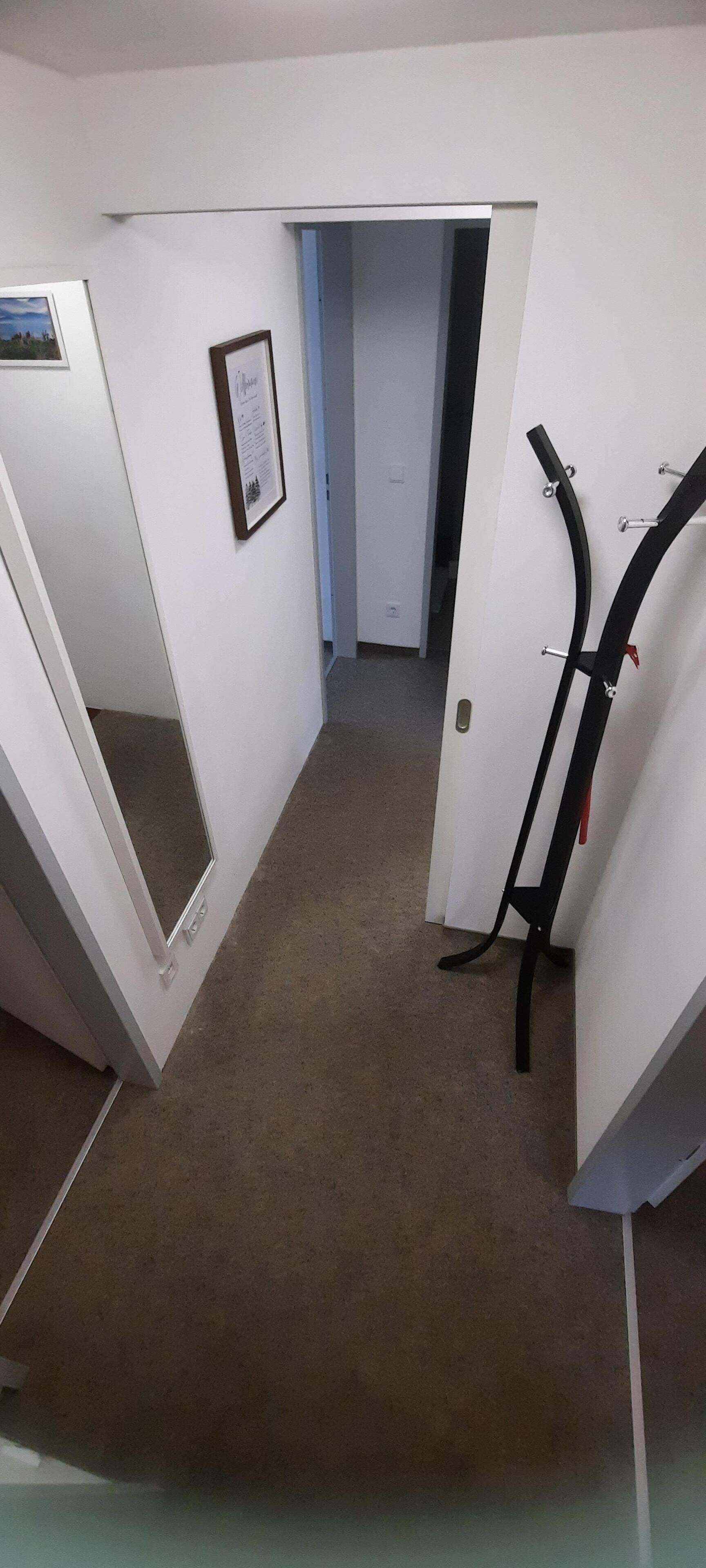 A narrow hallway with white walls, a framed certificate on the left, and a black metal rack on the right.