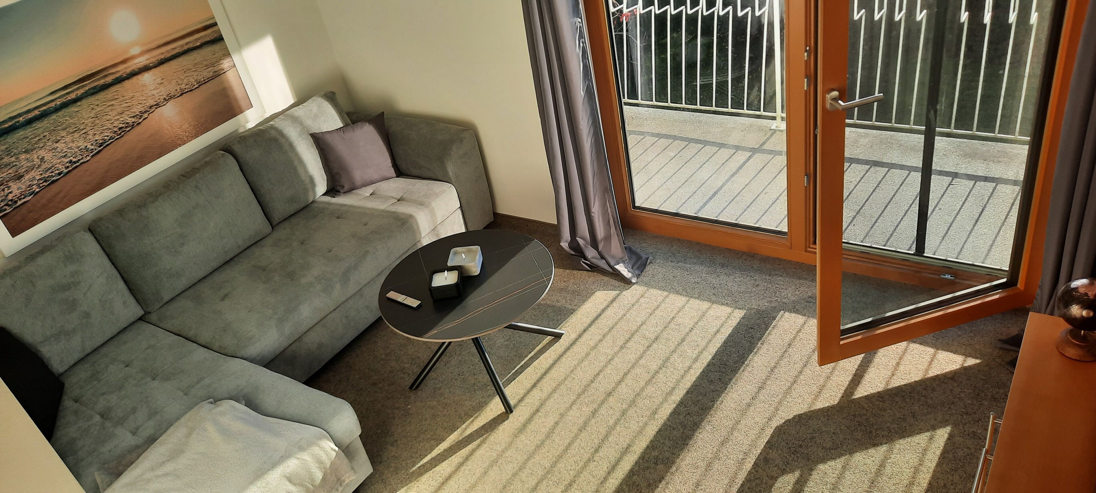 A modern living room with a grey sofa, a small black table, and a sliding glass door leading to an outdoor balcony.