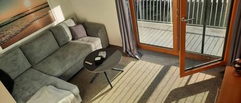 A modern living room with a grey sofa, a small black table, and a sliding glass door leading to an outdoor balcony.