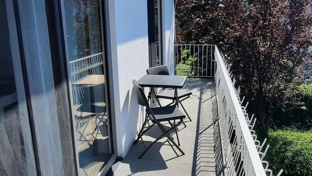 A balcony with a table and chairs, a glass door, and a white railing.