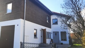 A two-story house with a dark brown roof, white walls, and a small front porch.