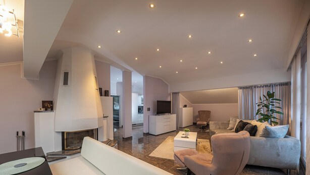 A modern living room with a sofa, armchair, and coffee table. There is a fireplace, a television, and a plant.