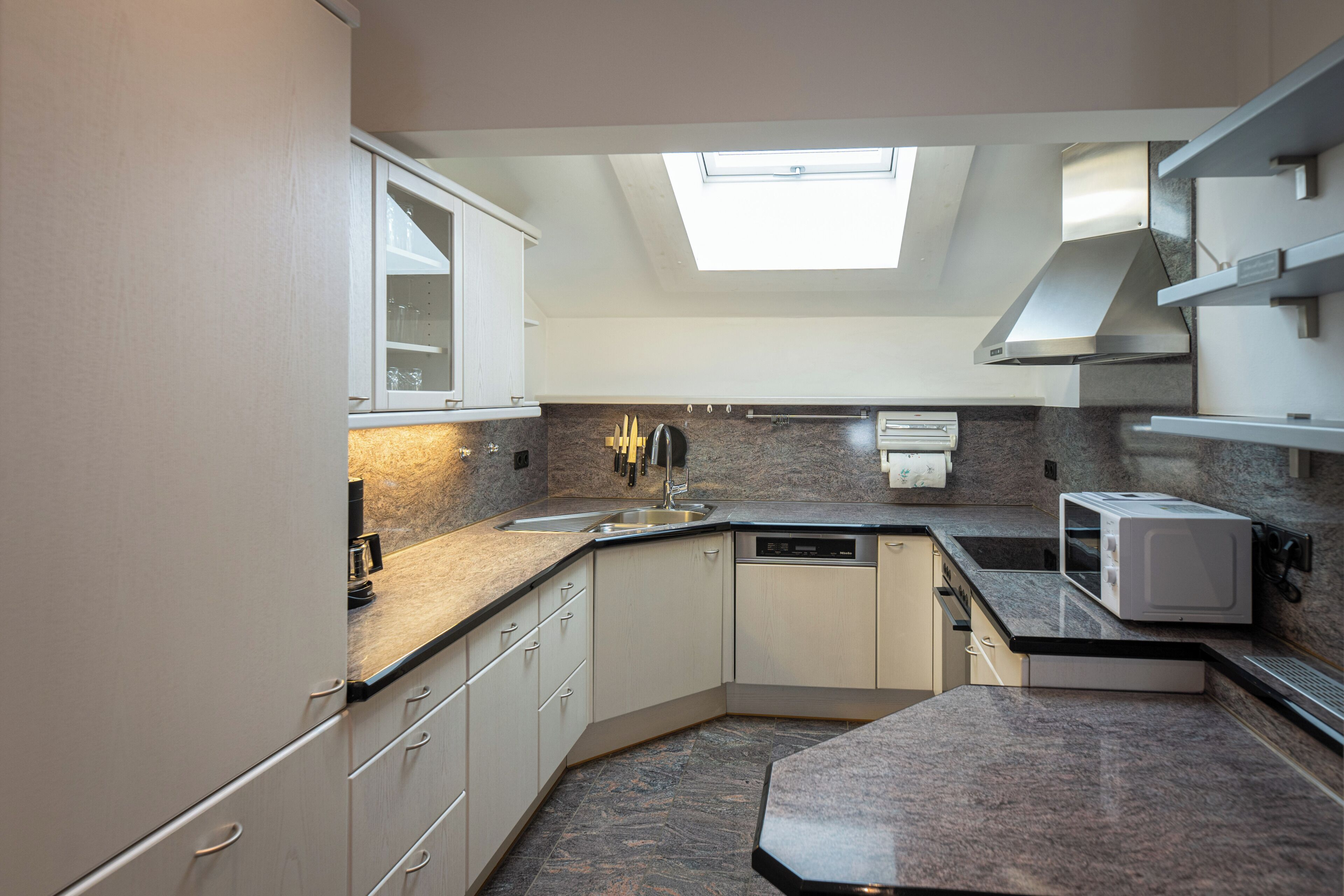 A modern kitchen with a skylight, granite countertops, and built-in appliances.