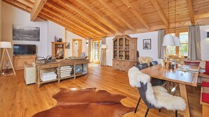 Une pièce spacieuse avec un plancher en bois, un plafond haut, une table à manger avec des chaises, un téléviseur et un meuble.
