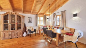 Un coin repas en bois avec un plafond haut, un meuble avec des portes en verre et un espace salon confortable.