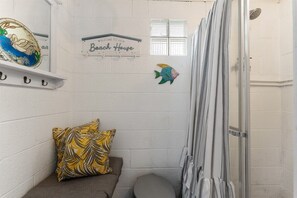 A small, enclosed bathroom with a shower, a towel rack, and a sign that reads 'Welcome to our Beach House.'