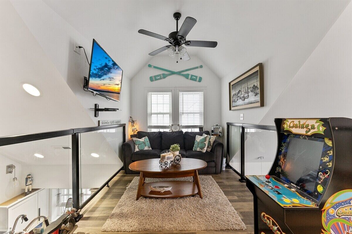 A living room with a flat-screen TV, ceiling fan, couch, coffee table, and arcade game.