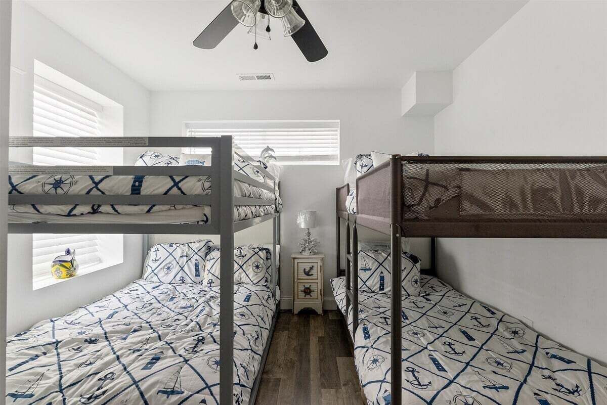 Une chambre avec un lit superposé, une literie sur le thème de la marine, un ventilateur de plafond et une petite table de chevet avec une lampe.