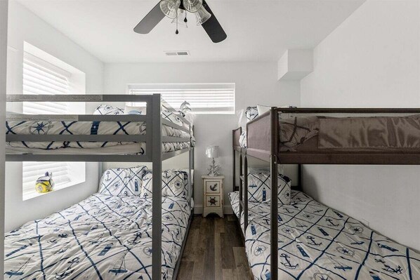 Habitación con literas, ropa de cama de temática náutica, un ventilador de techo y una mesita de noche con lámpara.