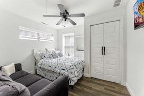 Un dormitorio con cama, ventilador de techo, armario y ventana con persianas.