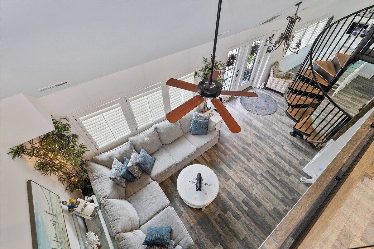 Un vaste espace de vie comprenant un ventilateur de plafond, un ensemble de canapés, une table basse et un escalier.