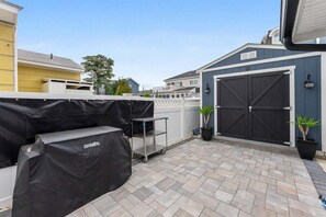 Ein überdachter Patio-Bereich mit Grill und Wagen, eine Garagentür und Kübelpflanzen.