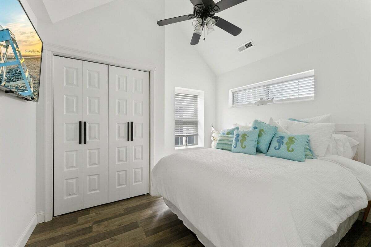 Une chambre à coucher avec un lit, un ventilateur de plafond, une armoire et une fenêtre avec des stores.