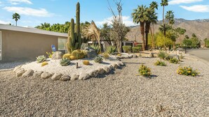 A desert garden with cacti, palm trees, and a building with a parking sign. - Azul Oasis by AvantStay | Pool, Hot Tub, Firepit, Bocce Ball | Mins to Downtown (Palm Springs)