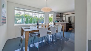 A modern dining area with a large table, white chairs, and a pendant light. - Azul Oasis by AvantStay | Pool, Hot Tub, Firepit, Bocce Ball | Mins to Downtown (Palm Springs)