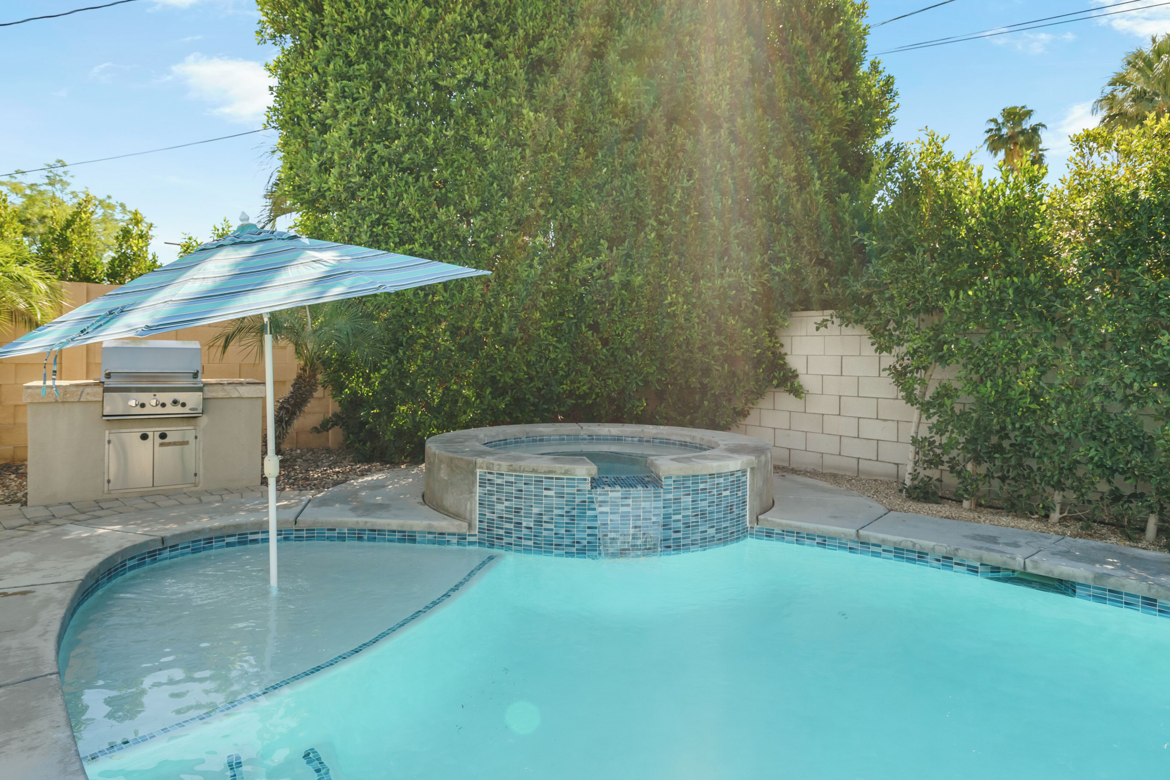 A swimming pool with a hot tub, a grill, and a patio umbrella.