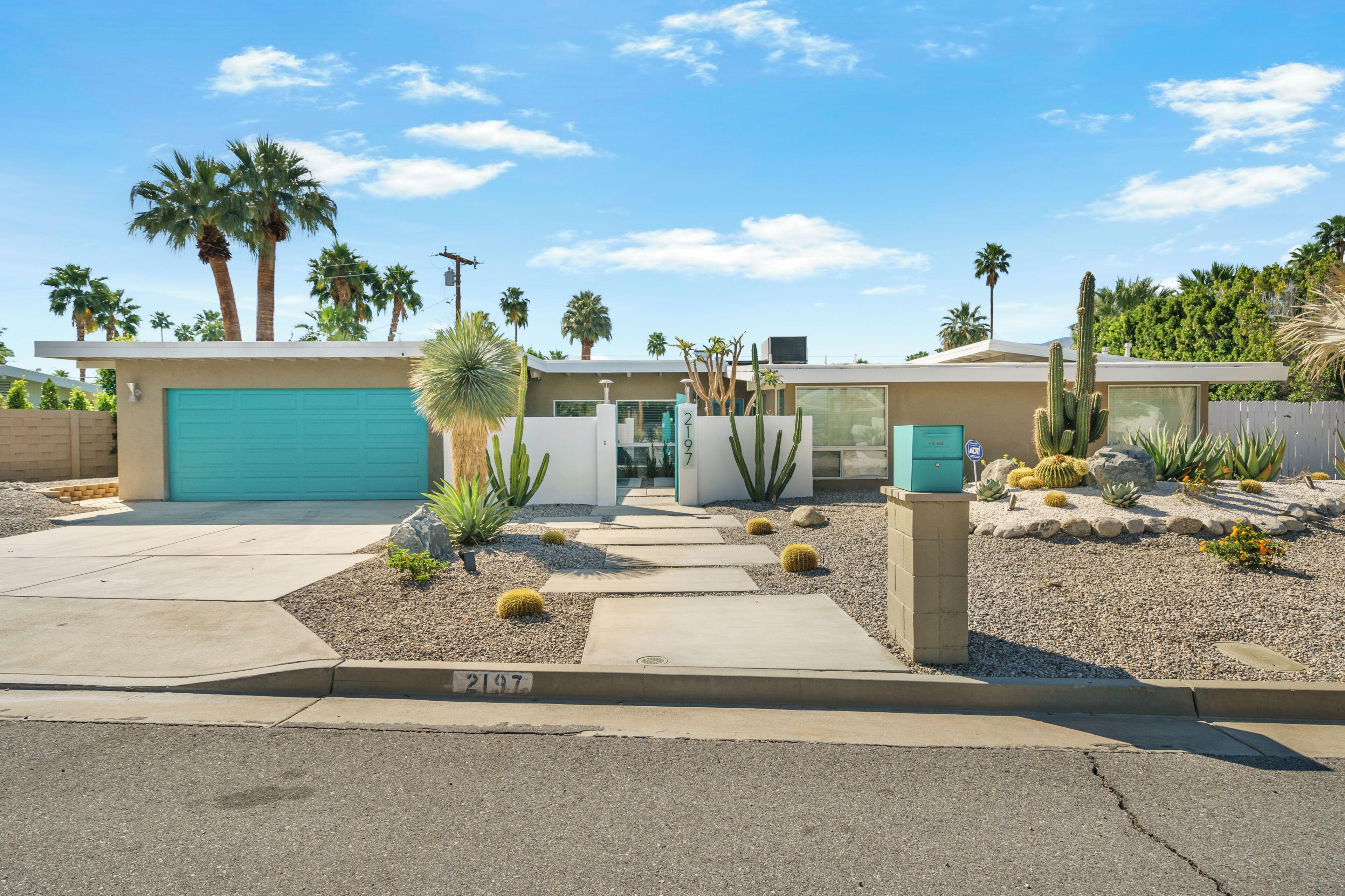 A modern house with a garage, palm trees, and cacti in the yard.