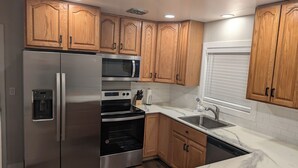 A modern kitchen with wooden cabinets, stainless steel appliances, a marble countertop, and a window with blinds. - Beautiful home in Idaho Falls (Idaho Falls)