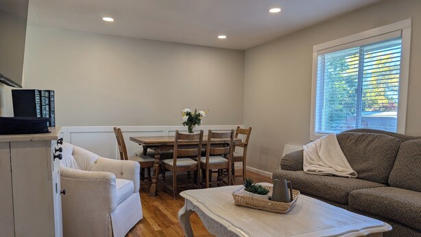A cozy living room with a wooden dining table, two chairs, a white sofa, and a white armchair. A coffee table with a basket and a pitcher is in the center. - Beautiful home in Idaho Falls (Idaho Falls)