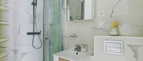 Ein Badezimmer mit Duschkabine, Waschbecken mit Spiegel darüber und einer kleinen Ablage für Toilettenartikel.