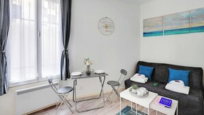 A modern living room with a sofa, a dining table, and a view of the outdoors. - Comfortable studio - 2P -  Necker (Paris)