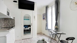A modern kitchen with a tiled backsplash, a flat-screen TV mounted above the counter, and a dining area with a table and chairs. - Comfortable studio - 2P -  Necker (Paris)