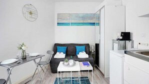A compact living space with a kitchenette, a dining area, and a sofa with a view of the sea. - Comfortable studio - 2P -  Necker (Paris)