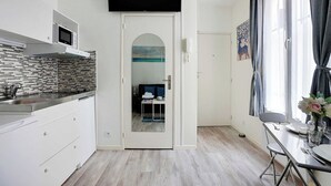 A modern kitchen with white cabinets, a microwave, and a tiled backsplash. There is a dining area with a table and chairs, and a door leading to a living space. - Comfortable studio - 2P -  Necker (Paris)