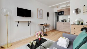 A modern living room with a flat-screen TV, a dining table with chairs, a kitchen area with a microwave, and a sofa with a green throw blanket. - Peaceful Studio -2P- Moulin Rouge (Paris)