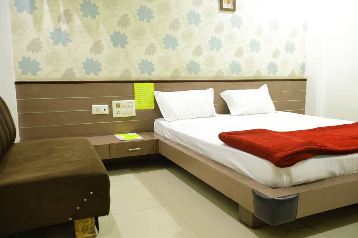 A bedroom with a bed, a nightstand, a brown chair, and a wall with floral wallpaper.